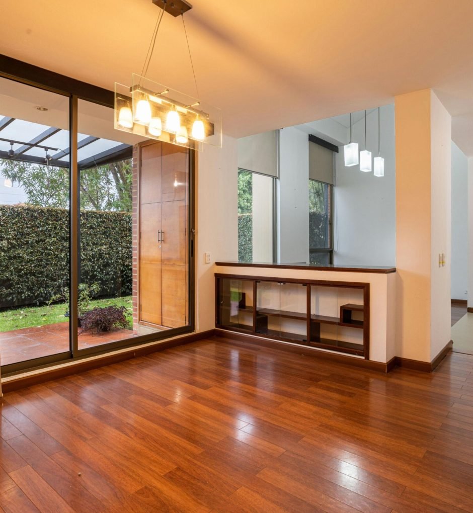 Bright minimalist living space with wooden flooring and glass doors leading outside.
